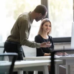 Collega's laten elkaar op de computer zien hoe je efficiënt uren kan noteren in het programma Project Hours.
